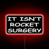 Neon sign with colorful letters reading 'It Isn't Rocket Surgery' quote.