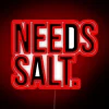 Neon sign that reads 'Needs Salt' in bold colorful letters