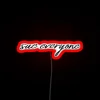 Lit up with attitude, 'Sue Everyone' neon script warning sign.