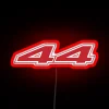 Formula 1 driver Lewis Hamilton in his Scuderia Ferrari 2025 racing gear, illuminated by a glowing neon RGB sign in red.