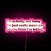 A vibrant neon sign displaying "Not Joking I'm Mean" with RGB lighting in pink.