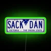 A neon sign displaying a license plate with 'Sack Dan' in RGB colors, green version. Image.