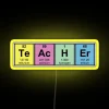 Science teacher holding a neon RGB sign displaying chemical elements in vibrant yellow colors.