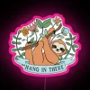 Colorful sloth hanging from a neon sign with the phrase 'Hang in there' written above it.