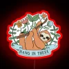Sloth hanging from a colorful neon sign with the phrase 'Hang in There' written above it.