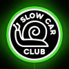 Neon sign with slow car club logo in green on a black background.