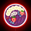 Vibrant purple acai smoothie bowl with colorful fruits on a neon-lit background.
