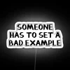 Neon sign with colorful letters reading 'Someone Has to Set a Bad Example'