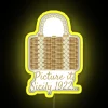 A woman's wicker purse in the foreground with a neon sign featuring a bright yellow background and RGB lights reflecting o...