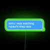Neon sign with colorful RGB lighting reflecting off a TV screen displaying RuPaul's Drag Race.