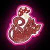 Kitten standing in front of a neon RGB sign featuring a large mushroom with pink accents.