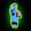AFL player Steph Catley with an AFL ball near a neon sign at night, sporting a green outfit.
