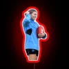 Australian Rules footballer Steph Catley posing with an AFL ball in front of a neon sign.