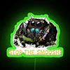 Close-up of a neon-lit, green-colored stop sign featuring a cute, jumping spider design.
