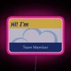 Neon pink nametag with bold, cursive font on a background of glowing RGB lights in a supermarket or retail setting.