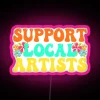 Neon sign reading 'Support Local Artists' in bold, colorful letters.