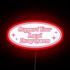Neon sign with colorful letters reading "Support Your Local Drag Queen" in bold, rainbow font.