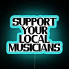 Neon sign with colorful letters spelling out support for local musicians in a vibrant city atmosphere at night.