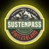 Neon sign in front of the Susten Pass mountain range at sunset.