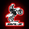 Red Suzuki DR-Z motorcycle performing a wheelie in front of a neon sign.