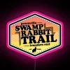 Neon sign on swamp rabbit trail with pink glow in a vibrant, colorful urban landscape.