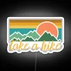 Neon sign reading 'Take A Hike' in bold, colorful letters against a dark background.