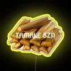 Neon sign reading 'Tamale Season' with vibrant yellow letters in a colorful city street setting.
