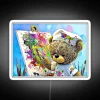 A colorful neon sign featuring a smiling teddy bear with bright RGB lighting, set against a white background.