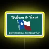 Tall, illuminated "The Texas Way" sign on the side of a drive in Texas with a yellow background and neon RGB lights.