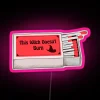 Neon sign with bold, cursive letters reading "This Witch Doesn't Burn" in pink against a dark background.