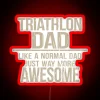 A father participating in a triathlon with a neon sign reading 'Triathlon Dad Like a Normal Dad Just Way More Awesome'