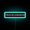Neon sign with bold, blue letters reading 'Troublemaker'