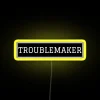 Neon sign reading 'TROUBLEMAKER' in yellow letters on a dark background.