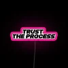 Neon sign with pink and blue lights reading 'Trust the process'