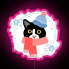 Tuxedo cat wearing winter outfit in front of a neon sign with pink accents.