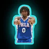 Tyrese Maxey of the Philadelphia 76ers poses in front of an RGB neon sign with a blue hue.