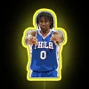 Philadelphia 76ers guard Tyrese Maxey standing in front of an RGB neon sign with yellow accents.
