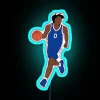 Philadelphia 76ers point guard Tyrese Maxey posing in front of an RGB neon sign with a blue hue.
