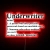 Insurance underwriter explained with humor, illuminated by neon sign in a brokerage setting.