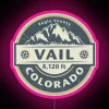Neon pink sign in Vail, Colorado, reflecting off snow-covered mountains at night.
