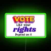 Neon sign with bold, colorful letters reading 'Vote Like Your Rights Depend On It' against a green background.