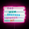 Neon sign featuring colorful, stylized family letters with pink accents in a modern cityscape.