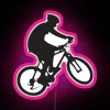 Rider performing a wheelie on a mountain bike in front of a neon sign with pink accents.