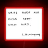 Neon sign with bold, cursive letters reading 'Write hard and clear about what hurts'
