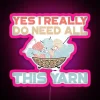 Close-up of a colorful neon sign with LED lights, featuring a humorous message about yarn needs.