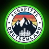 Panorama of Germany's Zugspitze mountain at sunset with a neon sign in the foreground.